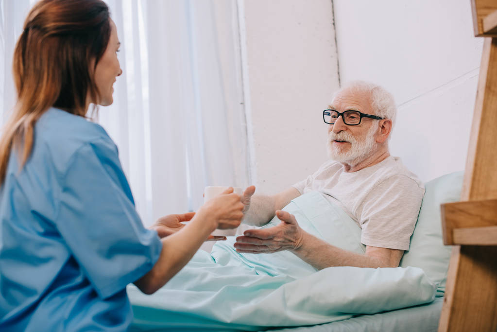 stock photo nurse helping senior patient bed hold cup