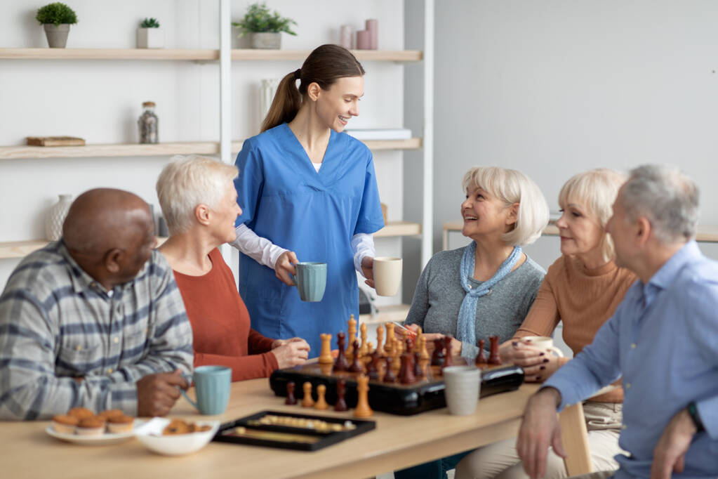 friendly nurse holding mugs, talking to elderly people, serving tea