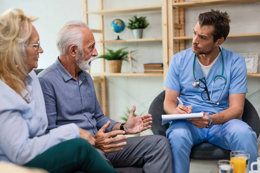 doctor taking notes while listening senior patient during home visit.