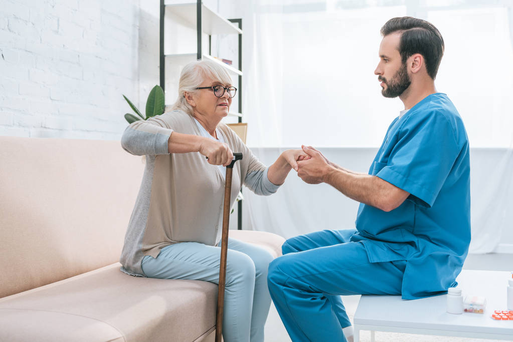 stock photo side view male nurse helping senior woman walking stick