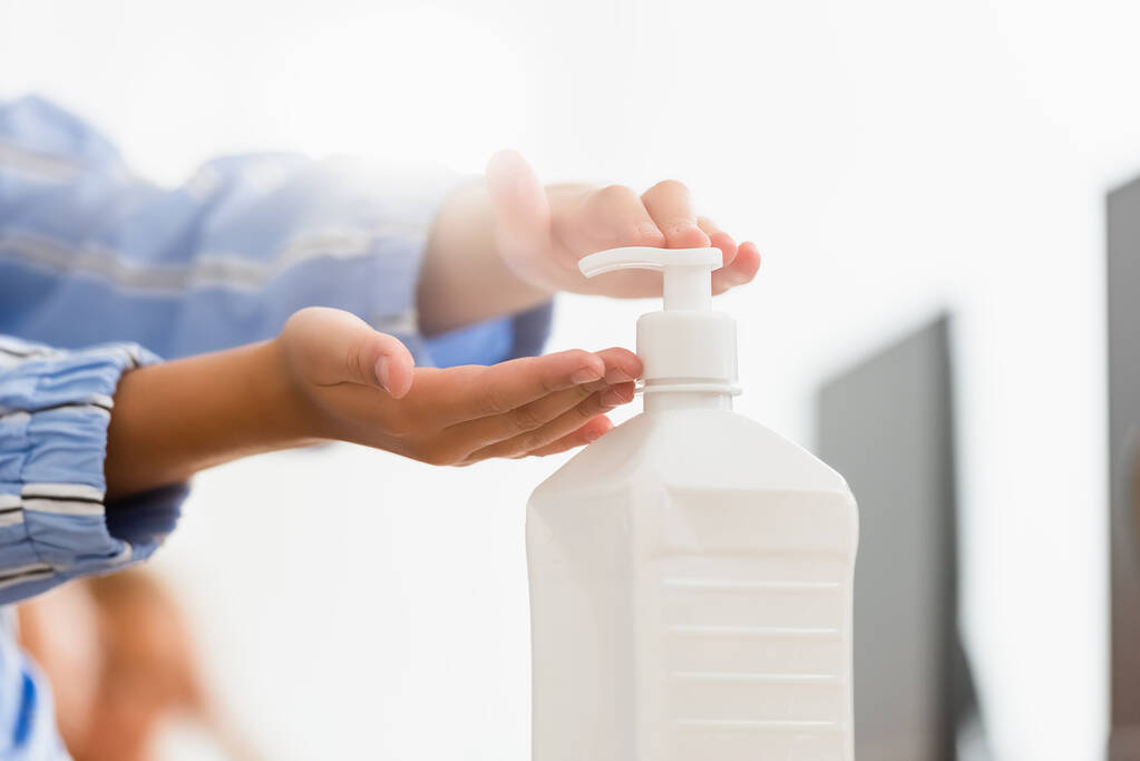 Hands pressing a white pump dispenser to dispense hand sanitizer or soap.